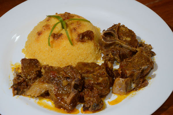 Prato de cuscuz nordestino moldado acompanhado de carne de bode cozida ao molho em um prato branco.